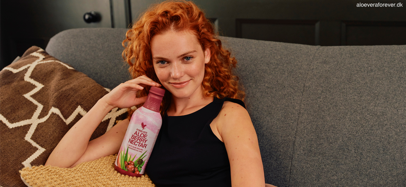 Aloe vera drikken Forever Aloe Berry Nectar i 1 liter PET flaske holdes op mod kinden af rødhåret kvinde