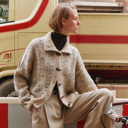 Ava Jacket fra My Favourite Things Knitwear stylet på model – oversize strikjakke i sandfarvet alpaca- og tweedmix med avismønster og duffelknapper.