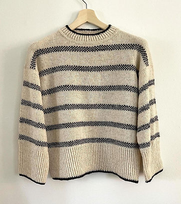 NORD Pullover af Hanne Rimmen hænger på en træbøjle. Strikket i råhvid bundfarve med sorte striber.