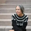 Siddende model iført anne Ventzels Selene Sweater i mørk brun og hvidt mønster