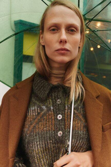 Tæt portræt af model iført Alma Sweater fra Knitthing_, hvor polokraven, knapstolpen og de flerfarvede jacquarddetaljer fremhæves. Fra Isager Archives 2