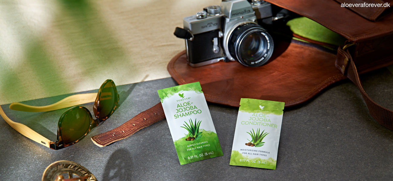 Vareprøver på Aloe-Jojoba Shampoo og Aloe-Jojoba Conditioner ligger på bord ved siden af solbriller og kamera