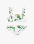 En todelt badedragt med tropisk blad- og blomsterprint. Overdelen har brede, flæsede stropper og en firkantet halsudskæring; underdelen har et enkelt, klassisk snit. Baggrunden er råhvid.