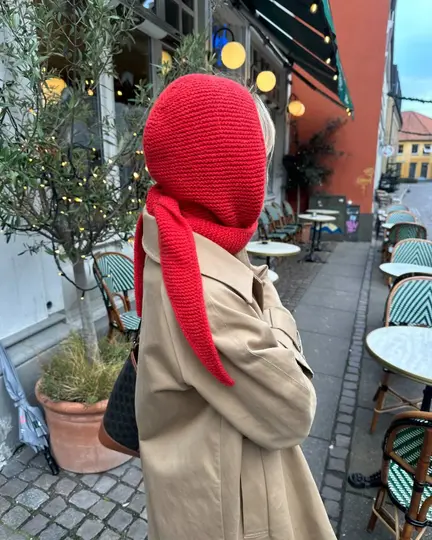 Sophie Hood fra PetiteKnit i rød cashmere, båret over beige frakke, hætten dækker hoved og hals, set fra siden og bagfra.