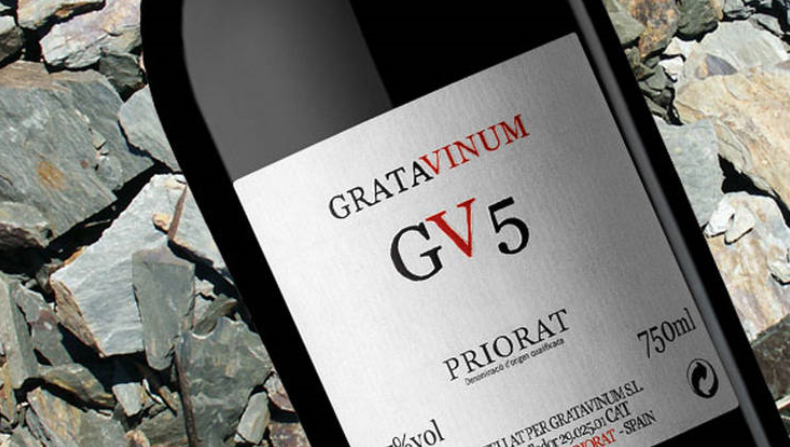 Der er zoomet ind på lablen på den økologiske rødvin Gv5, som kommer fra Gratavinum i Priorat. Lablen er hvid med sort og rød skrift. I baggrunden ses nogle sten som viser Gv5s jordbundsforhold.