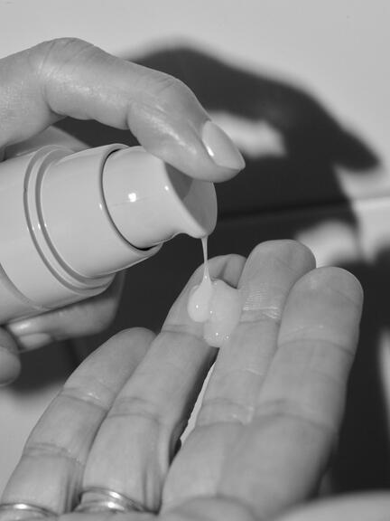 Acai All in One serum fra Rudolph Care punpes ud på fingrene af en velplejet hånd