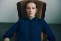 model sidder i stol ifoert moerkeblaa strikket otti cardigan designet af helga isager strikket i isager garn