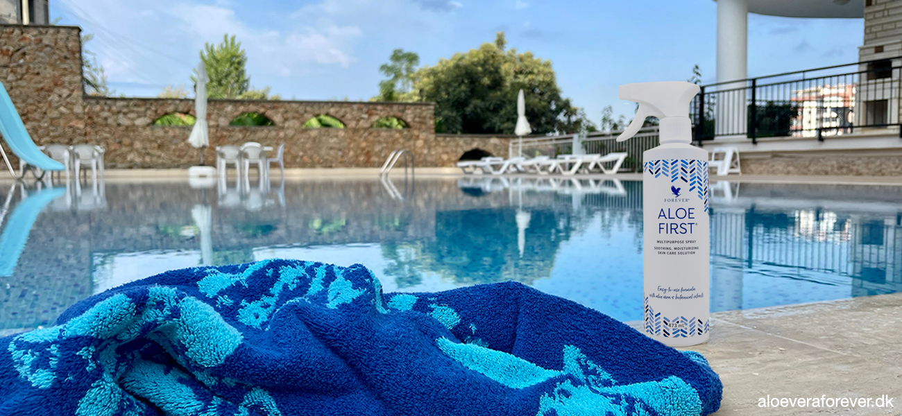 Forevers spray Aloe First står på poolkanten med et blåt håndklæde foran