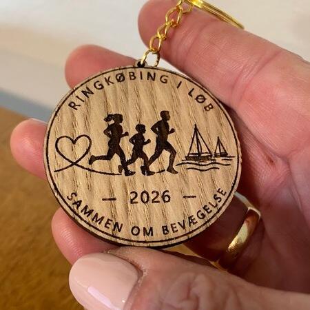 Rund Royal Run Ringkøbing 2026 nøglering i egefineret træ med løbere og sejlbåde holdt i hånden