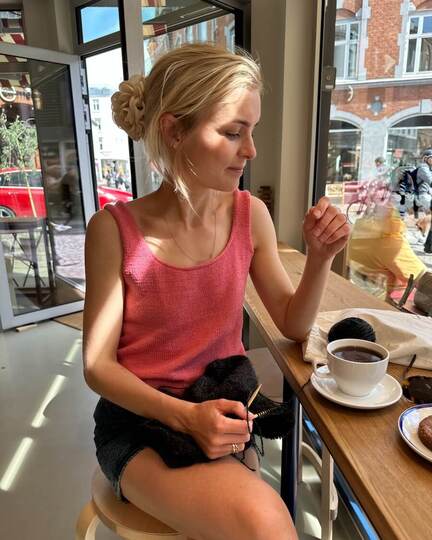 June Top Light – rosa strikketop stylet med sort nederdel på café