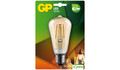 Emballage til en GP LED-lampe med en pære i vintage-stil med synlige filamenter. Emballagen inkluderer energieffektivitetsdetaljer, der viser 470 lumen og 37W tilsvarende. Baggrunden har grønne og orange nuancer med et billede af en tændt pære.