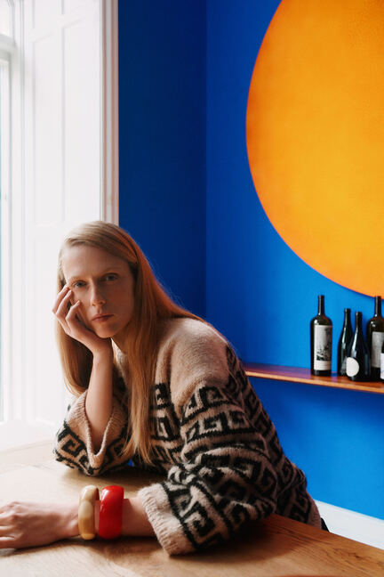 Athene Sweater af PetiteKnit fra Isager Archives 2 i beige og sort mønsterstrik, vist på model ved bord.