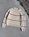 Festival Sweater fra PetiteKnit lagt fladt på grå fliser, strikket i lys bundfarve med striber i mint, pink og bordeaux.