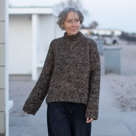 Model i brunmeleret Jilli Jam sweater strikket i Isager-garn på strandpromenade.