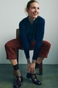 model sidder paa skammel ifoert moerkeblaa strikket otti cardigan designet af helga isager strikket i isager garn