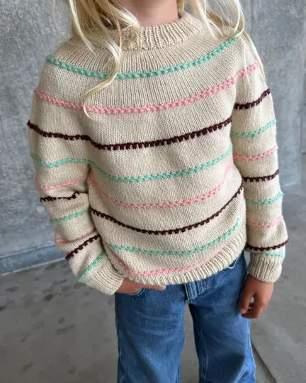 Barn iført Festival Sweater fra PetiteKnit med lysegrå bund og striber i mint, pink og bordeaux, kombineret med blå jeans.