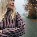 Person iført Edda Sweater, designet af Hanne Rimmen til Isager Archives 2, i farverne Wine (bundfarve) og Oak/Stone (mønsterfarver). Efterårsstemning på stille vej i baggrunden.