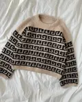 Athene Sweater strikket i Isager Soft, beige bundfarve e6s med sort fv. 30 grafisk mønster, vist liggende fladt på lys baggrund.