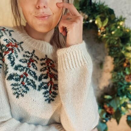 model sidder foran julekrans ifoert strikket kristtjoern christmas sweater designet af hanne rimmen