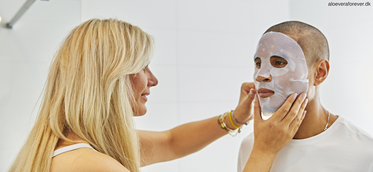 En kvinde lægger en aloe bio cellulose mask på en mands ansigt