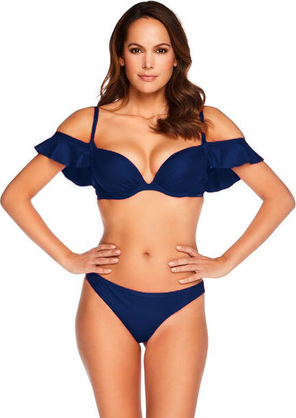 En kvinde iført en marineblå bikini med flæsede skulderstropper står med hænderne på hofterne og kigger ind i kameraet.