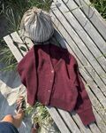 Scarlet Cardigan – strikket PetiteKnit cardigan i vinrød uld, lagt på bænk i sollys.