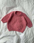 Baby iført Esther Sweater Baby fra PetiteKnit strikket i strukturmønster i rosa Sunday garn