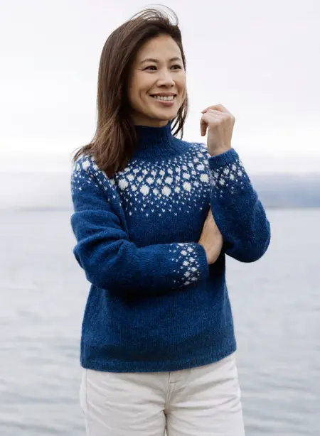 Kvinde ifoert bla Snjokorn sweater med hvid baerestykke-monster, strikket i Fjallalopi fra Istex.