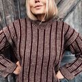 Edda Sweater designet af Hanne Rimmen i Wine som bundfarve og Oak/Stone som mønsterfarver. Personen står foran en rå trædør med hænderne i siden.