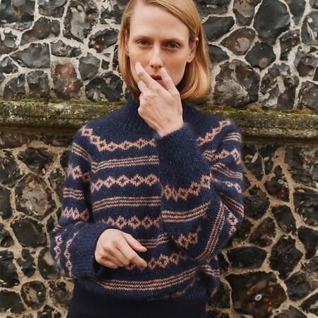 Mikala Sweater i navy og rosa mønster stående foran murværk – set forfra.