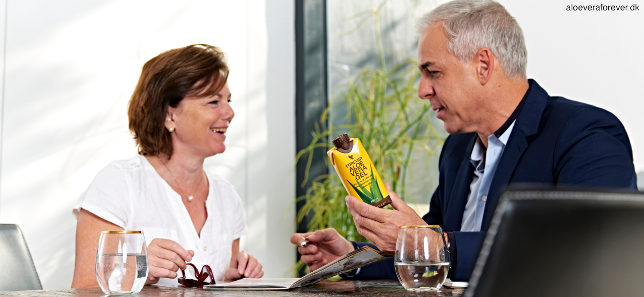 En kvinde og en mand sidder ved bord med en mini Forever Aloe Vera Gel og taler om Forever Living