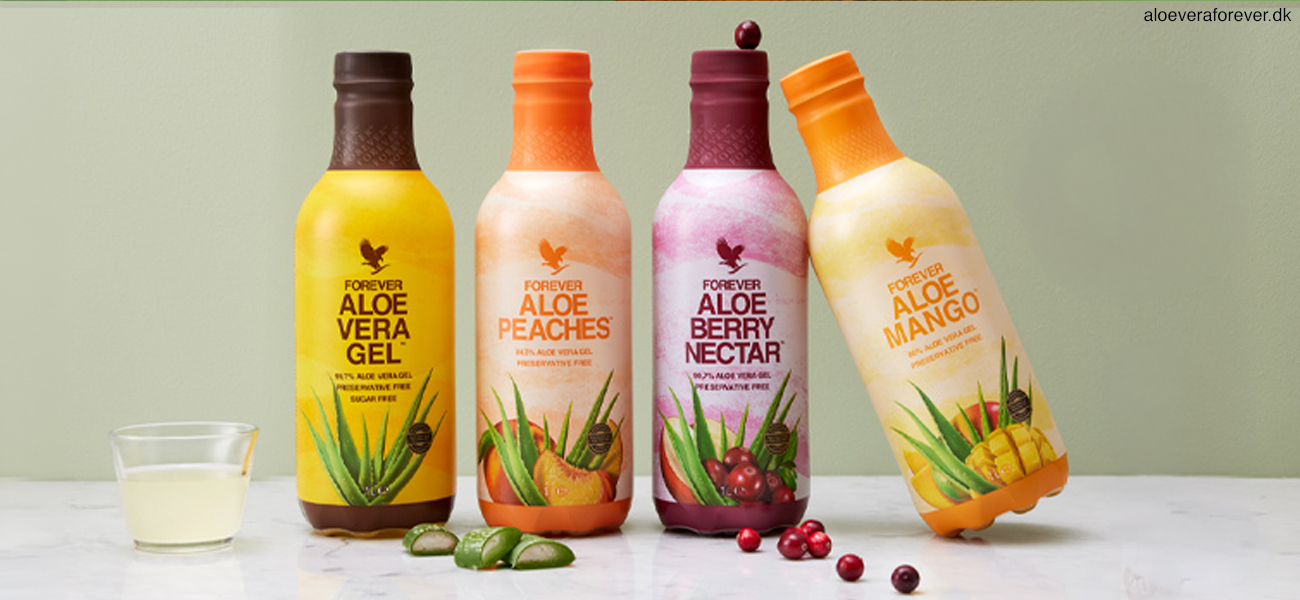 De fire slags Aloe vera gel fra Forever Living på hvidt bord med et lille glas Aloe Vera Gel, nogle afskårne Aloe vera blade og lidt tranebær