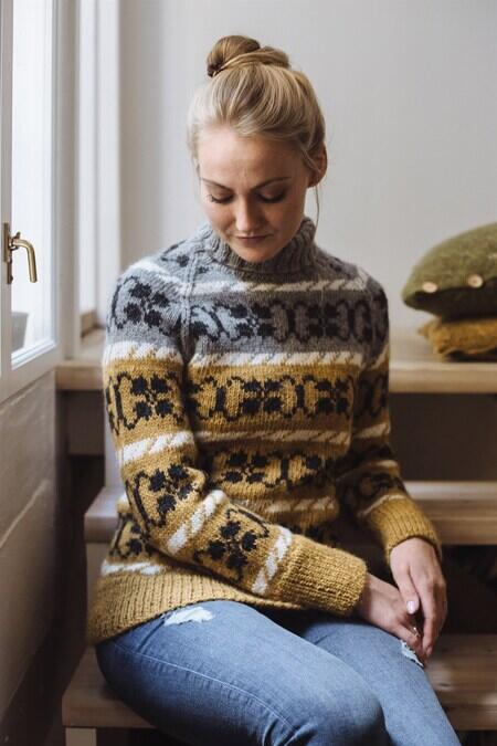 kvinde ved vindue iført klematis sweater fra camarose strikket i grå, hvid og gul lamauld