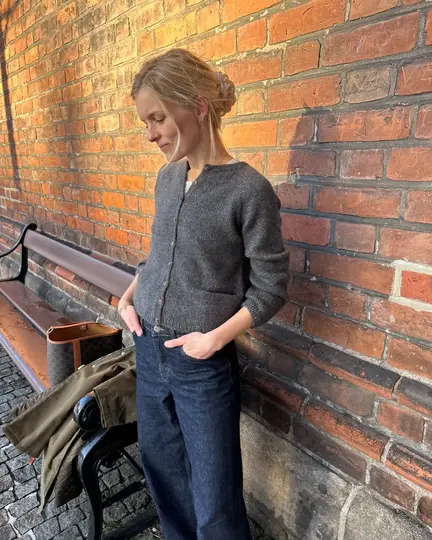 Copenhagen Cardigan fra PetiteKnit i grå, strikket i Alpaca 2 og Silk Mohair, stylet afslappet med jeans foran murstensvæg.