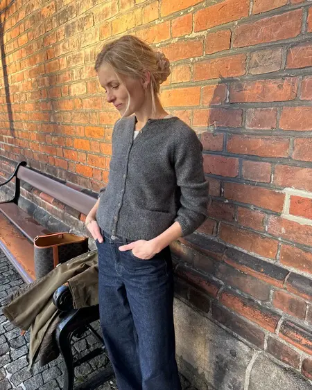 Copenhagen Cardigan fra PetiteKnit i grå, strikket i Alpaca 2 og Silk Mohair, stylet afslappet med jeans foran murstensvæg.