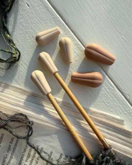 Pindebeskyttere fra PetiteKnit i brug, sat på strikkepinde for at sikre masker under pause i strikkearbejdet