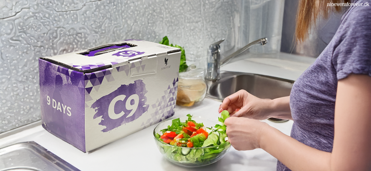 C9 boks på køkkenbord. Kvinde tilbereder råkostsalat.