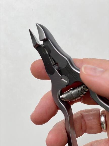 Negleklipper holdes i en hånd, parat til brug. Baggrunden er en enkel, hvid overflade, hvilket fremhæver præcisionsværktøjets metalfinish og konstruktion.