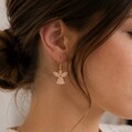Nærbillede af kvinde med engleøreringe i egetræ fra By Sandager. Elegante træøreringe med guldfarvet ørekrog og klassisk englemotiv – lette smykker inspireret af nordisk design.