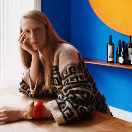 Athene Sweater af PetiteKnit fra Isager Archives 2 i beige og sort mønsterstrik, vist på model ved bord.