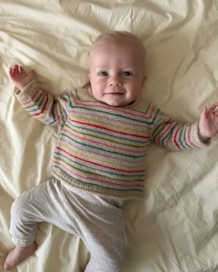 Baby iført Frankie Sweater Baby fra PetiteKnit strikket med raglan og smalle farverige striber