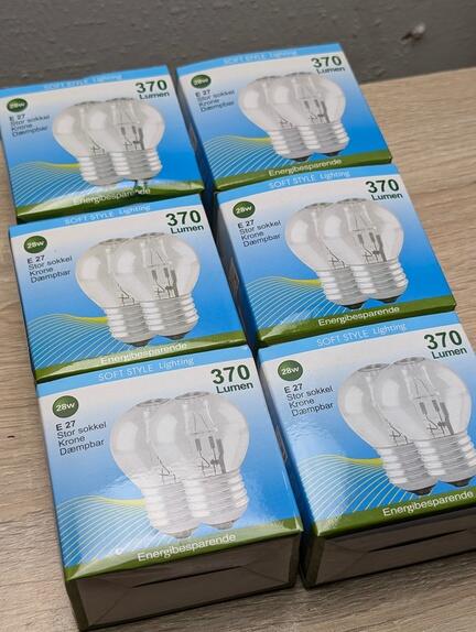 Seks kasser med energibesparende pærer er anbragt på en træoverflade. Hver æske er mærket 370 Lumen og E 27 Sokkel, med en illustration af pæren indeni.