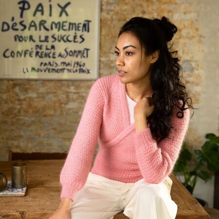 Model sidder på et bord iført strikket cardigan Embrace fra filcolana i Vilja og Tilia i Lyserød 370 Flamingo