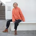 Model sidder iført orange Jilli Jam sweater med bred raglan og høj hals.