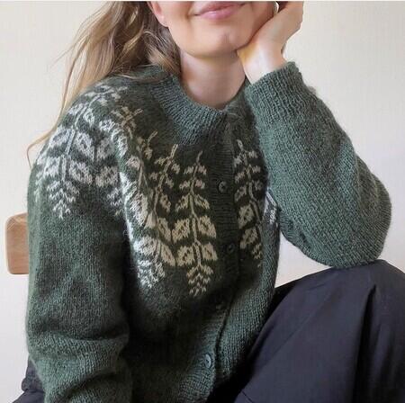 Kvinde sidder iført KRISTTJØRN CARDIGAN Hanne Rimmen Strikkekit grøn og lys Dansk Pelsuld 8-2 hjelholt