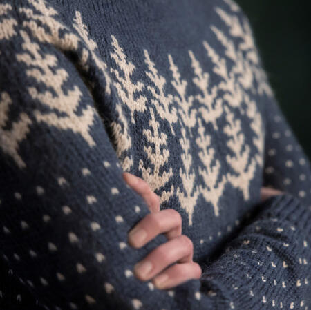Nærbillede af mønsterdetaljer i Let it Snow sweater af Hanne Rimmen – grantræer og snefnug i naturhvid på mørkeblå bund.