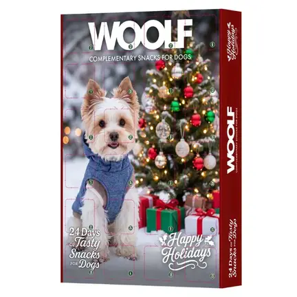 WOOLF Julekalender til hunde med lækre godbidder under de 24 låger. På kalenderens forside ser man motivet af en hund, der hygger sig foran et pyntet juletræ.