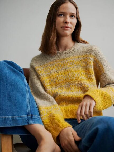 Kvinde iført Johanne Loop Sweater fra Other Loops i sand og gul, fotograferet siddende.