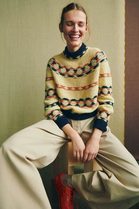 model smiler og sidder paa stol ifoert helga isagers sweater gunta i gul version med isager soft