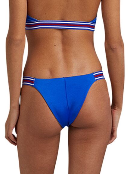 En person iført en blå bikini med hvide og røde striber på linningen, set bagfra, står på en ensfarvet baggrund.